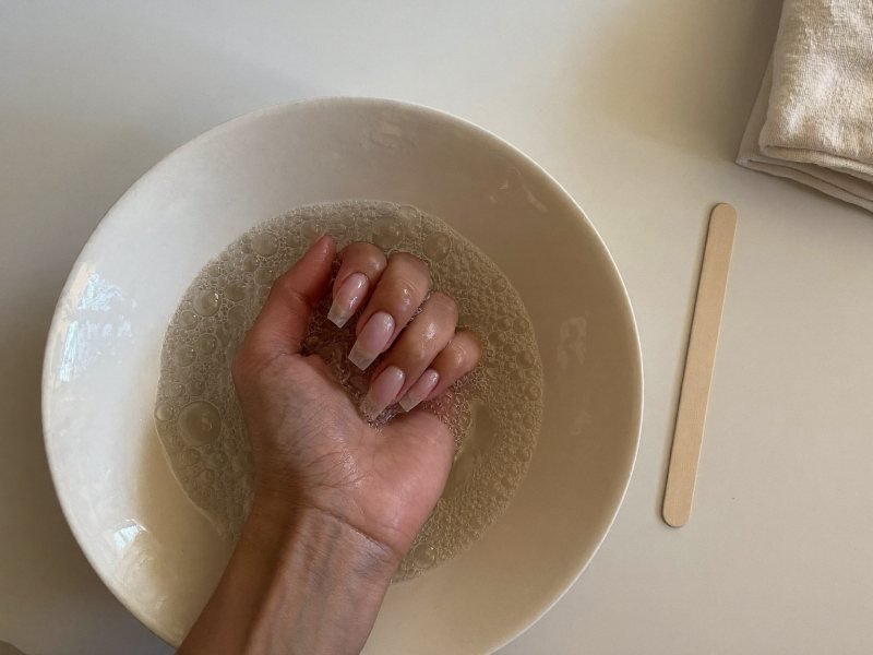 Fingertips soaking in a bowl of warm soapy water to remove press-on nails