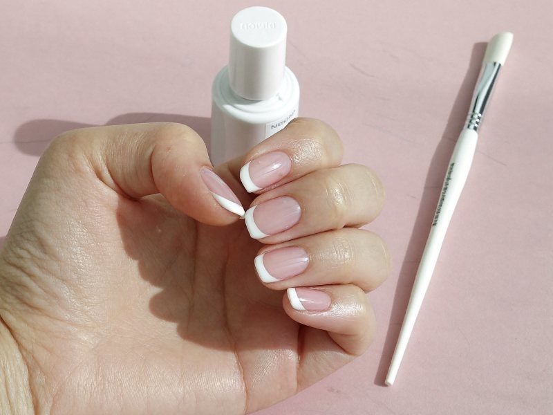 Finished French tips at home on short oval nails with polish bottles nearby