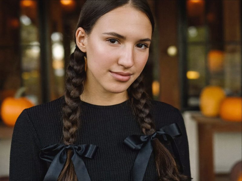 Halloween hairstyles: a woman with long dark hair in two sleek braids tied with black ribbon