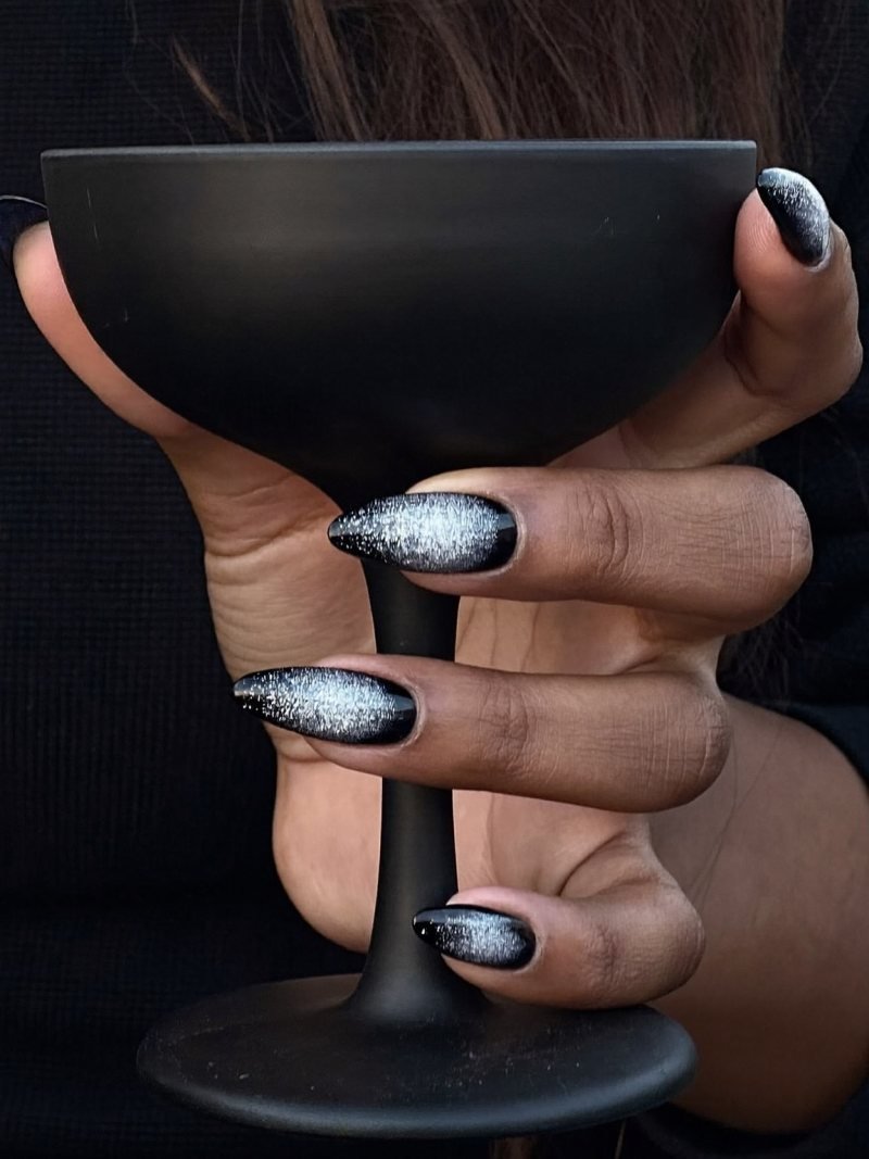 Long almond black nails fading into silver glitter at the tips