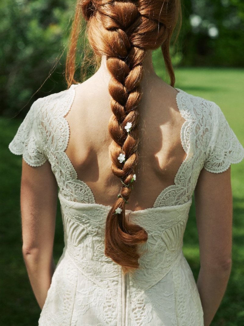 Long red hair in a loose fishtail braid with small white flowers