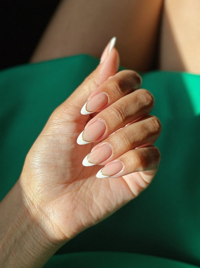 Medium almond French nails with a thin gold line and a green dress