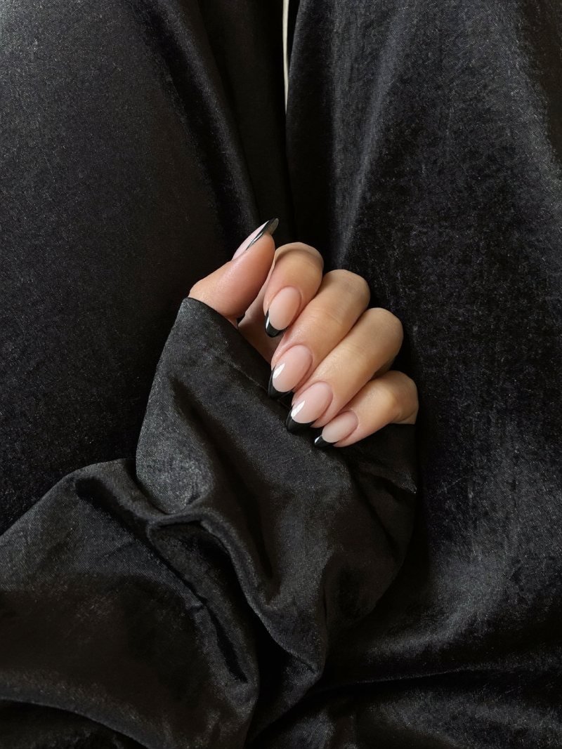 Medium almond nails with a nude base and glossy black French tips