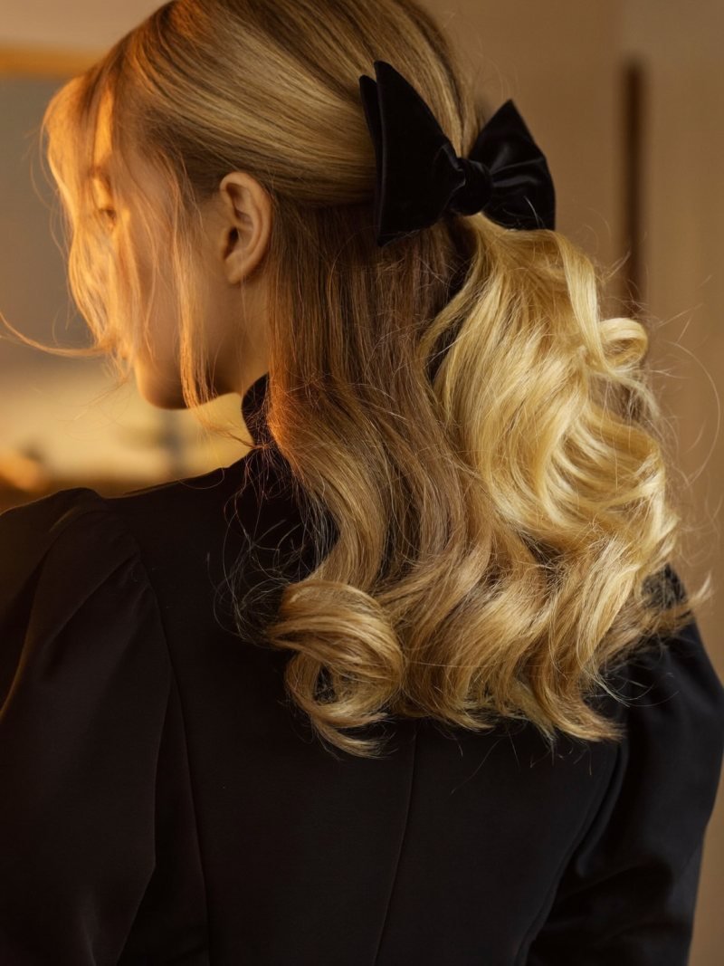Medium blonde hair worn half up with a black velvet bow
