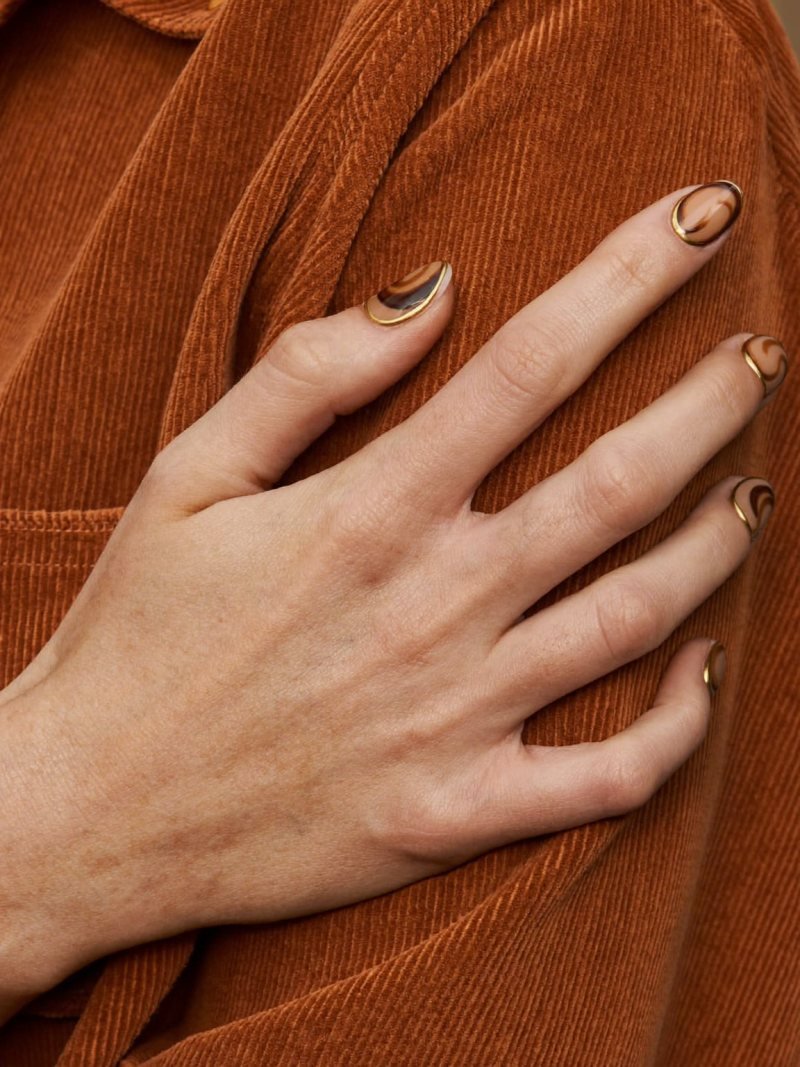 Medium oval nude nails with brown swirls edged in fine gold