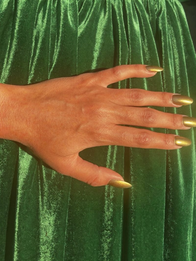 Short almond gold chrome nails with an emerald dress
