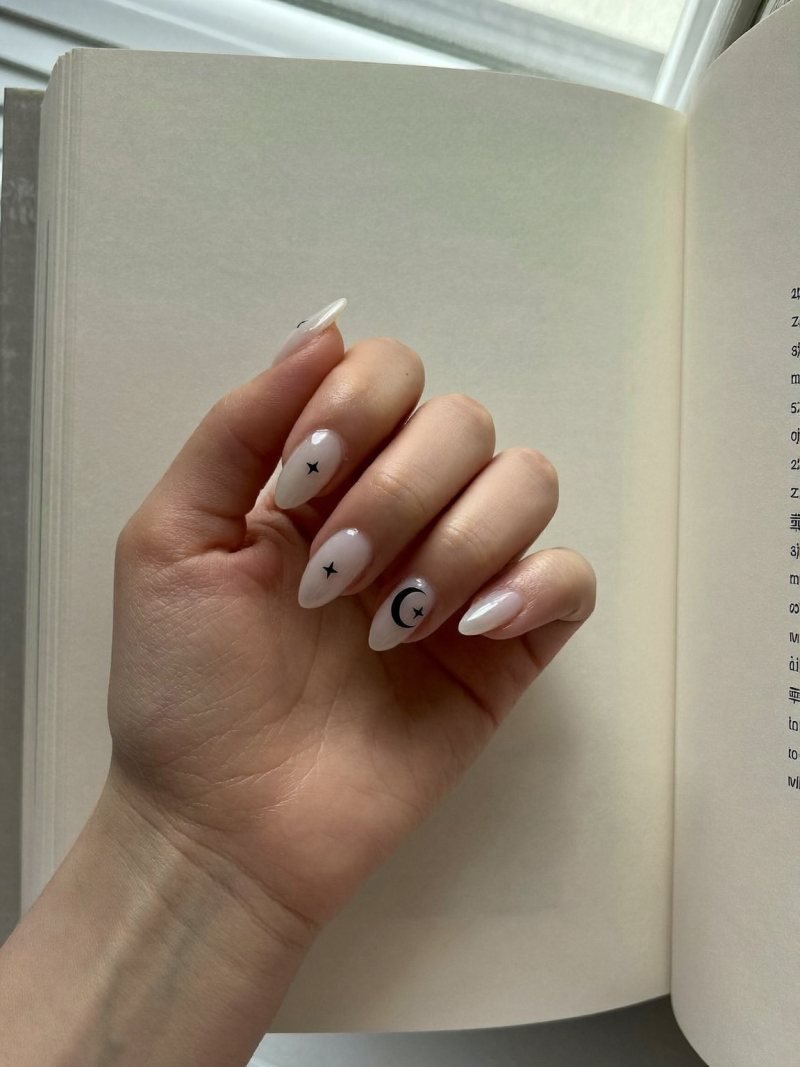 Short almond milky white nails with tiny black crescent moons and stars