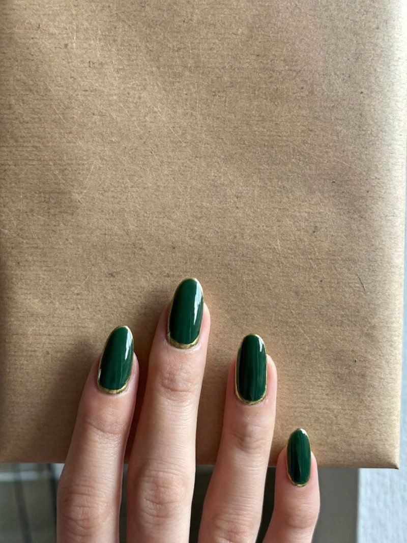 Short almond nails in forest green with a thin gold line at the cuticle