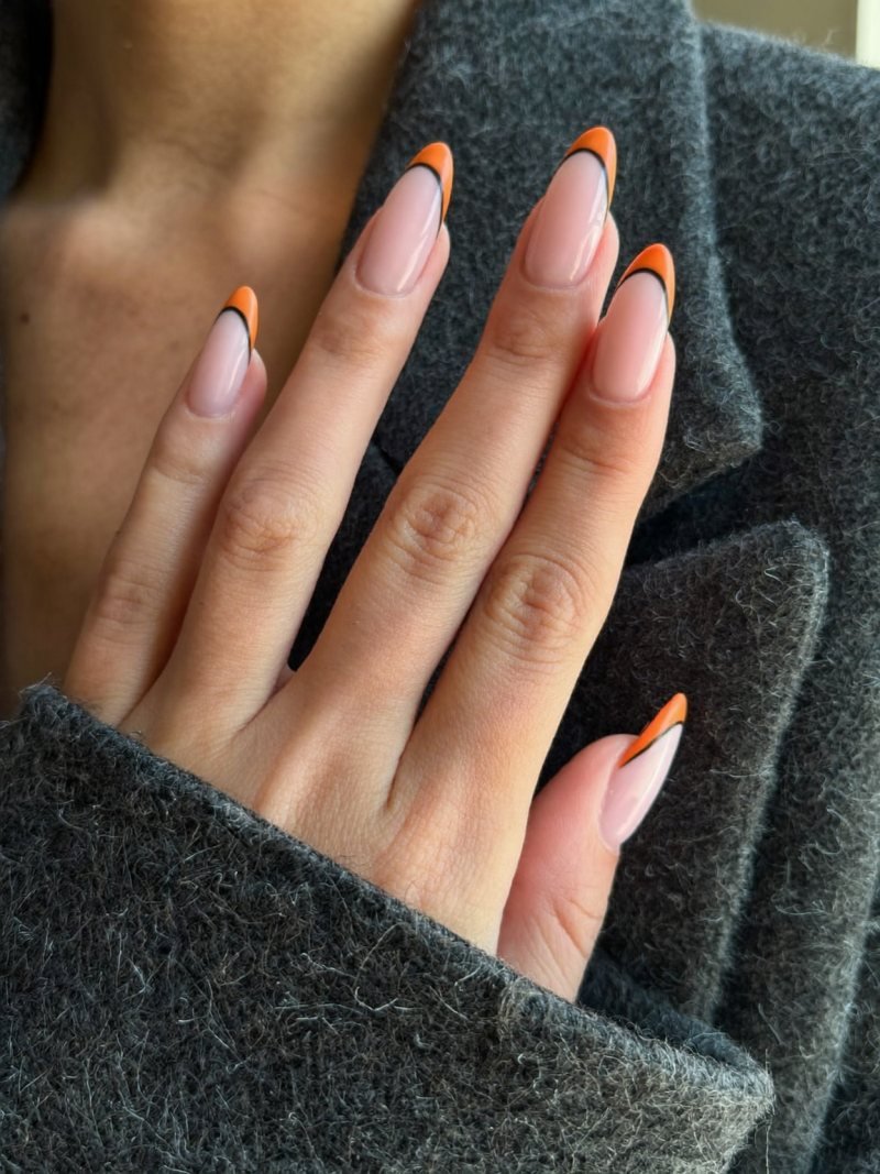 Short almond nails with a thin orange tip and a thin black line beneath it