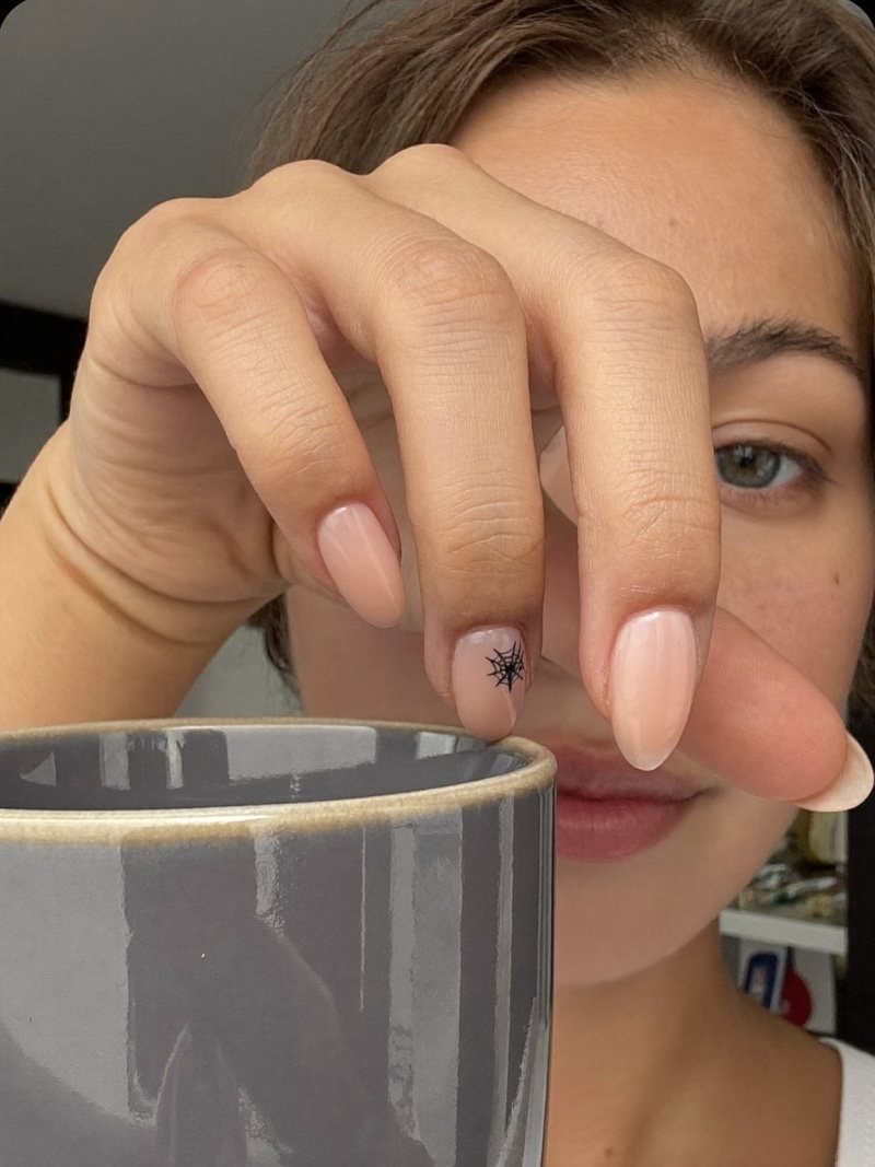 Short almond nude nails with a small black web in the corner of one nail