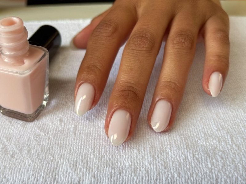 Short nails with a sheer pink base coat drying before French tips are added
