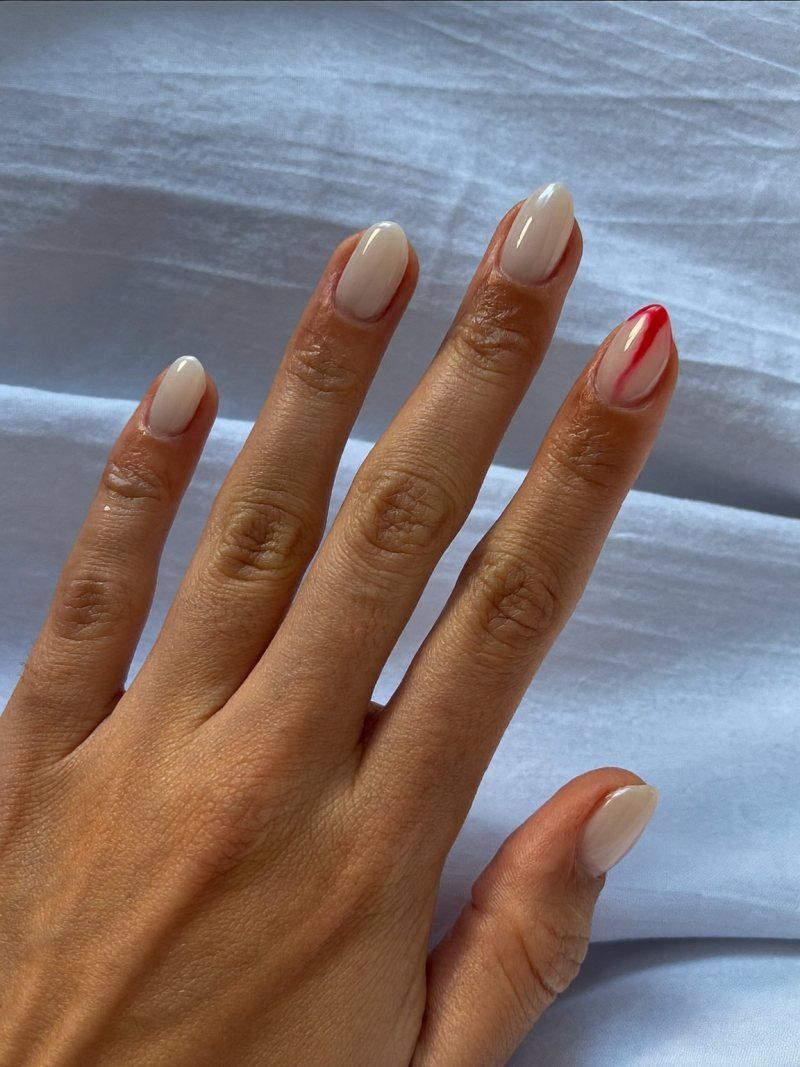 Short oval milky white nails with a small red drip on one nail