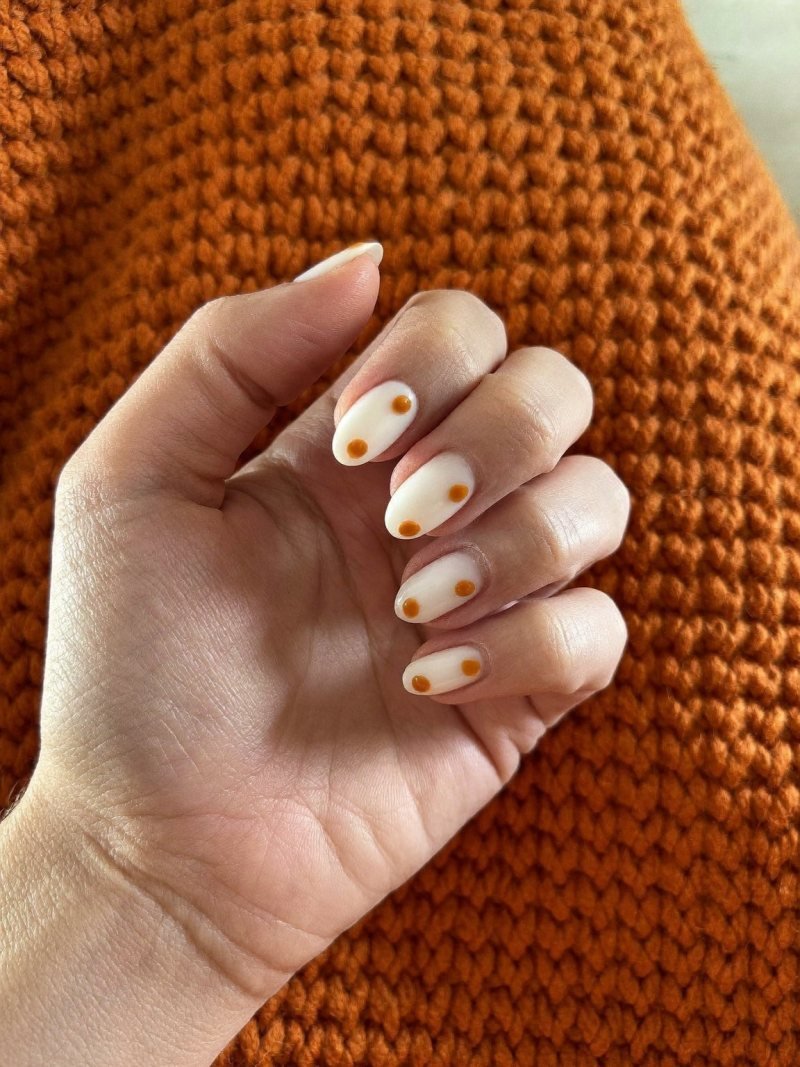 Short oval milky white nails with small orange dots
