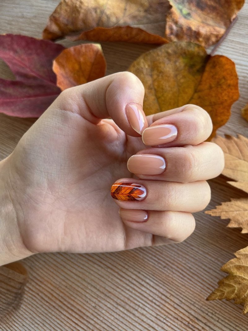 Short oval nude nails with one small hand-painted autumn leaf