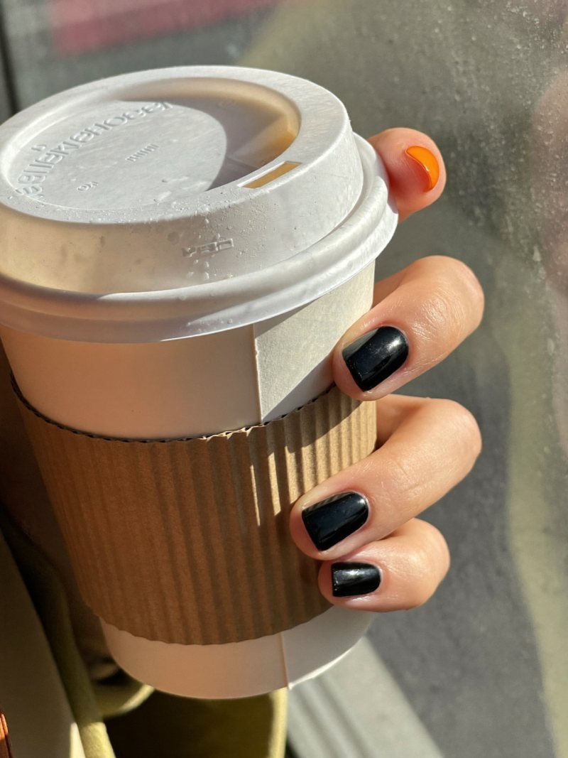 Short round black nails with one pumpkin orange accent nail