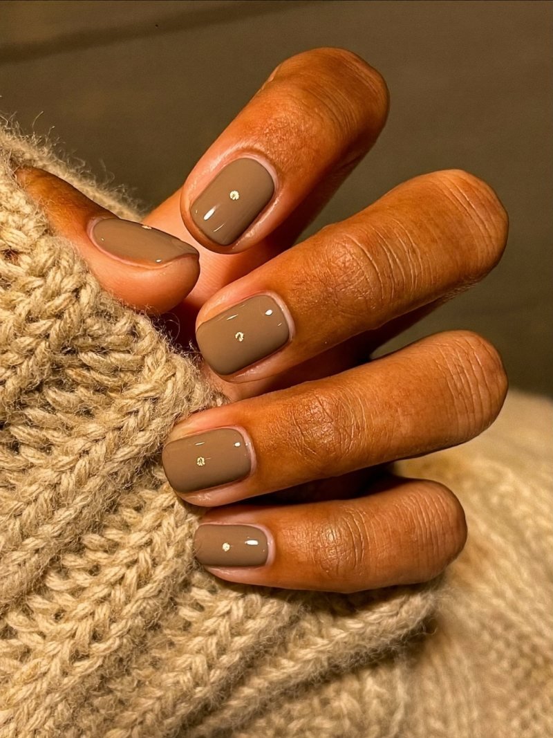 Short round mocha brown nails with a tiny gold dot at the base of each nail