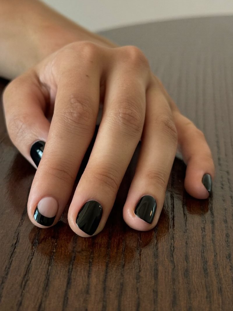 Short round nails with a black base and a bare half moon at the cuticle