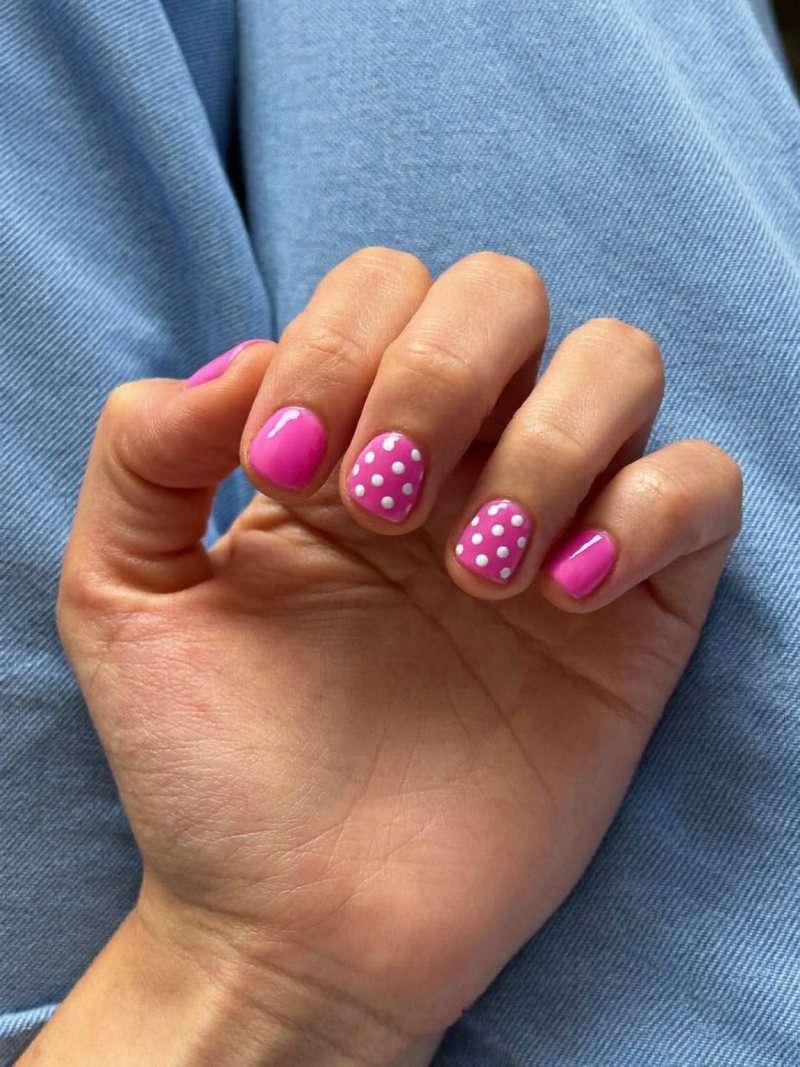 Short round pink nails with small white polka dots