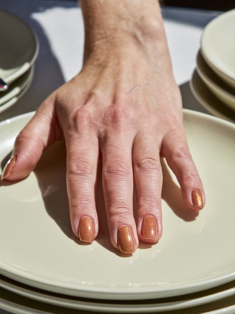 Short round toffee nude nails covered in fine gold shimmer