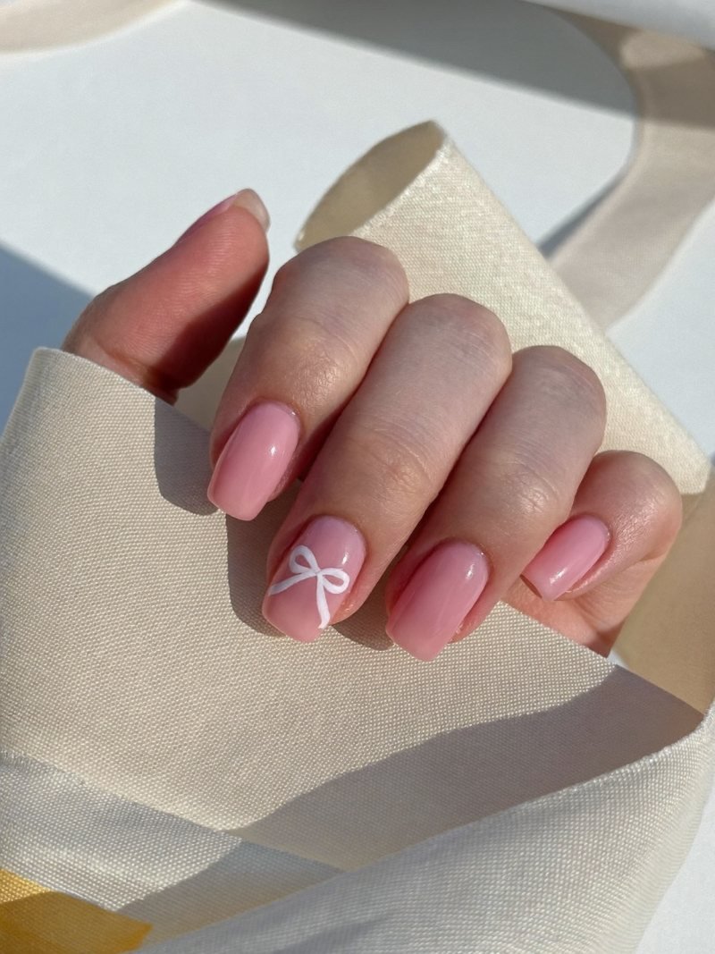 Short square nails in sheer pink with a tiny white bow on one nail