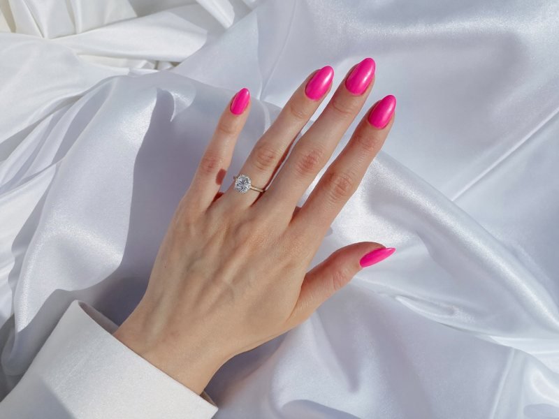 Short wedding nails in sheer pink with a diamond ring on white fabric