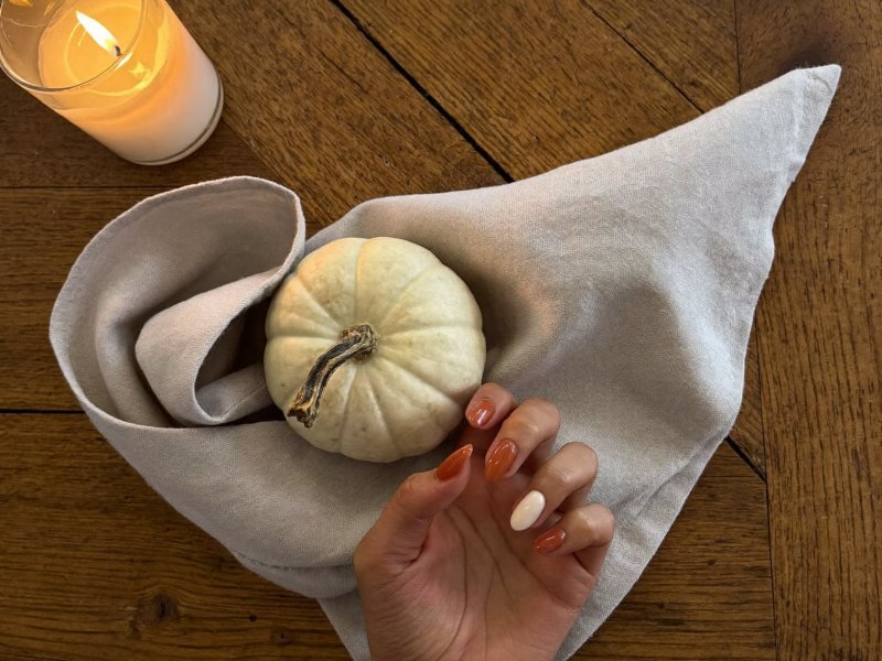 Simple Thanksgiving nails in rust orange and cream on a set dinner table