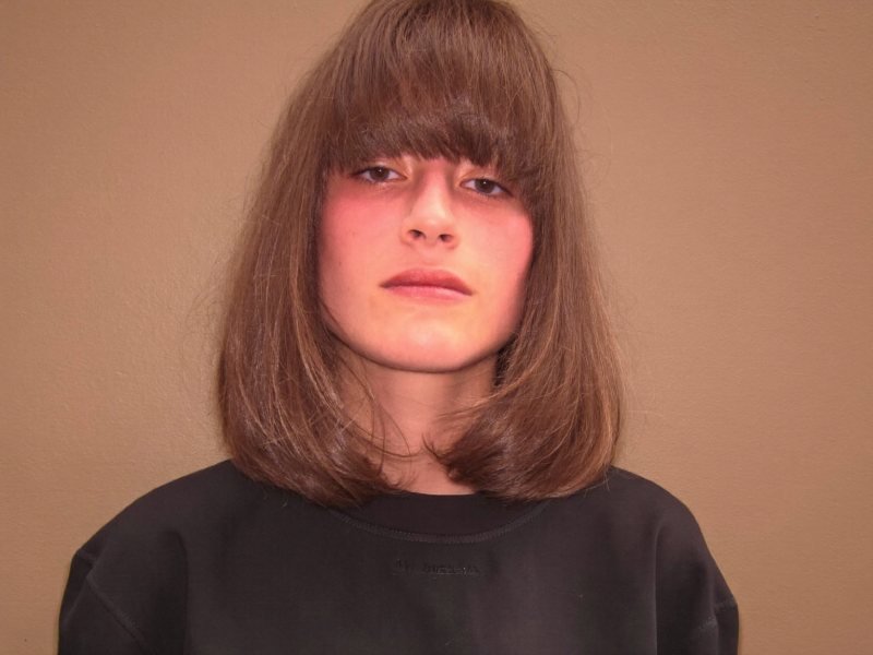 Types of bangs: a woman with shoulder-length brown hair and a full blunt fringe at the eyebrows
